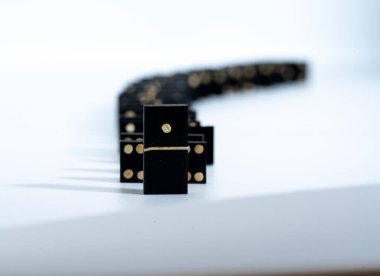 several black domino game tiles, forming a row. The first card is the one that corresponds to number one. They are on a white table.