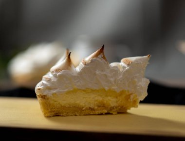 a slice of cake served on a yellow table. the cake is lemon pie, the meringue is in the form of cones on top of the delicious yellow lemon cream.