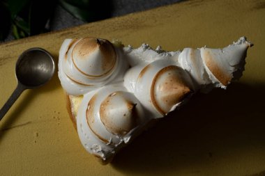 top view of a slice of cake served on a yellow board. the cake is lemon pie, the meringue is in the form of cones on top of the delicious yellow lemon cream.