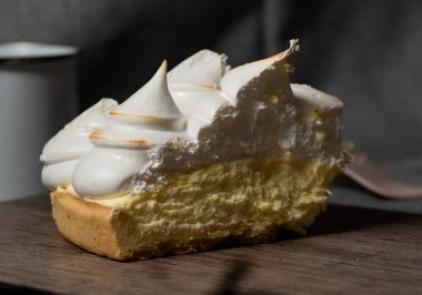 a portion of lemon pie, with lemon-flavored yellow cream and meringue cones on top. delicious cake on a wooden board.