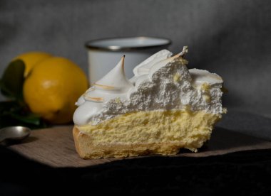 a portion of lemon pie, with lemon-flavored yellow cream and meringue cones on top. delicious cake on a wooden board. there are lemons and a white cup