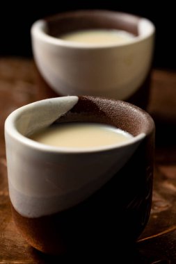 closeup of a shot glass with liquor, white and brown. It is very small and round in shape.