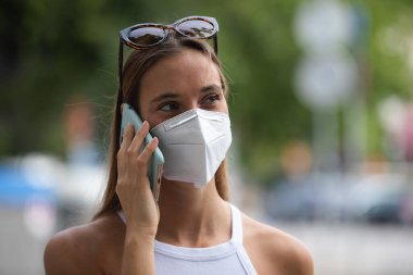 Tıbbi maske takan ve cep telefonuyla konuşan mutlu bir kadın. Koronavirüse karşı koruma (covid-19) salgını