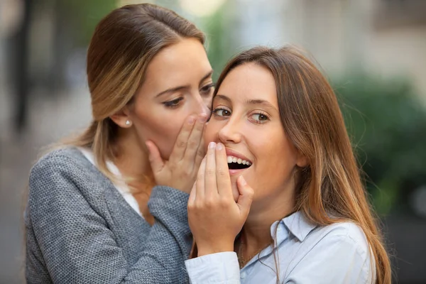 Beautiful woman whispers to her mate shocking news outdoors