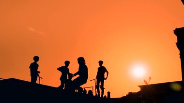 Yavaş çekim: Tanımlanamayan genç çocuk silueti kaykay parkında, turuncu gün batımı gökyüzüne karşı scooter 'da yüksek atlama numaraları gösteriyor. Spor, ekstrem, serbest stil, açık hava aktivitesi konsepti