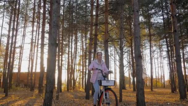Вид спереду: жінка їде на велосипеді в осінньому міському парку на заході сонця повільний рух — стокове відео
