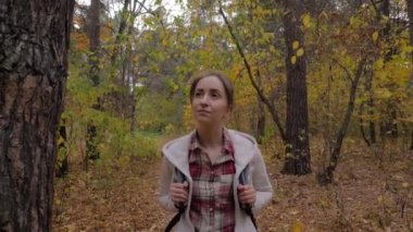 Sırt çantalı genç bir kadının sonbahar parkında yürüyüşünün ön görüntüsü.