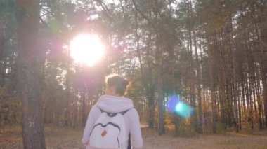 Sırt çantalı bir kadın sonbahar parkında yürüyor. Sabit çekim, güneş mercekleri parlıyor.