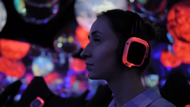 Mujer con auriculares inalámbricos en exposición o museo con luz colorida — Vídeos de Stock