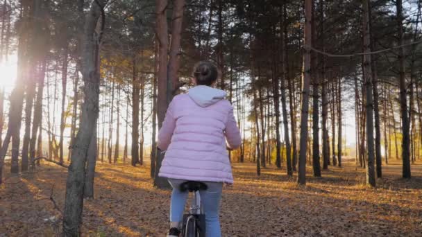 Ung kvinna rida cykel i höstens stadspark i solnedgången - slow motion — Stockvideo