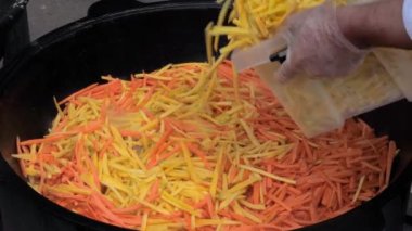 Şef pilav için patates ve havuç dilimleri pişiriyor, pilav ise büyük bir kazanda.
