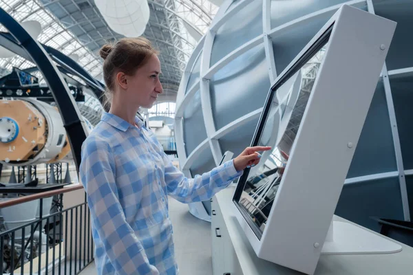 Woman touching interactive touchscreen display kiosk at exhibition - side view