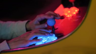 Woman gamer pushing buttons of retro arcade machine in dark room: close up