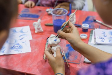 Professional woman potter painting ceramic penny whistle in pottery workshop