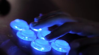 Woman gamer pushing blue buttons of retro arcade machine in dark room: close up