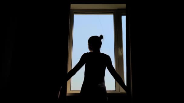 Silhouet van vrouw die gordijnen opent en uit het raam kijkt - achteraanzicht — Stockvideo