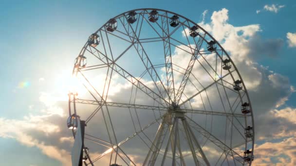 Silhouette of ferris wheel rotating against blue sky with clouds: sun lens flare — Stock Video