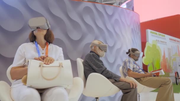 Grupa osób starszych korzystających z zestawu słuchawkowego wirtualnej rzeczywistości na wystawie technologii VR — Wideo stockowe