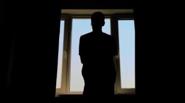 Adamın silueti perdeleri açıyor ve sabahları pencereden dışarı bakıyor.