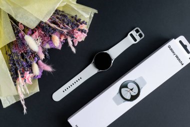 Minsk, Belarus - Eylül 2021: Samsung Galaksisi 'nin yeni pazarı akıllı saati beyaz bilezik, paket kutusu ve koyu arkaplanda bir buket kurutulmuş çiçek. Şık fotoğraf.