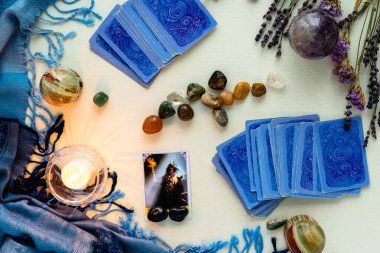 Minsk, Belarus - Şubat 2022: Tarot kehanetinde yer alan şeytan kartları, üzerinde mumlar ve taşlar bulunan kurumuş çiçekler ve mavi masa örtüsü olan bir masa örtüsü. Büyü ve okült