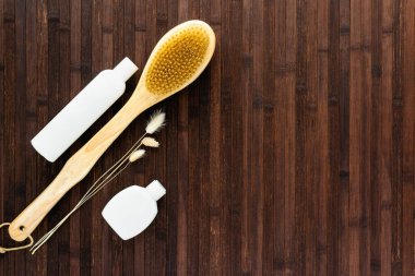 Karanlık bir ahşap masada boş beyaz şişeler, bir masaj fırçası ve kuru çiçekler var. Kozmetik cilt ve vücut bakımı, tedavi, gençlik koruma kavramı. Yatay fotoğraf.