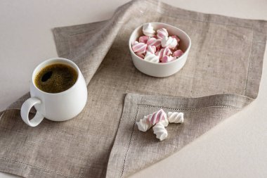 Beyaz porselen bardak, sıcak kokulu kahve ve gri bir peçetenin üzerinde marşmelov. Yatay fotoğraf.