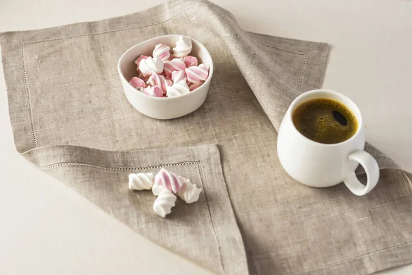 Gri keten bir peçeteye, beyaz bir kasede beyaz pembe bir şekere ve bir kupa kahveye. Yatay fotoğraf.
