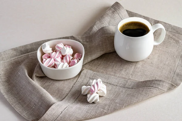 Sıcak kokulu kahve ve beyaz bir kâsede, peçetede servis edilen tatlı marşmelov. Yatay fotoğraf.