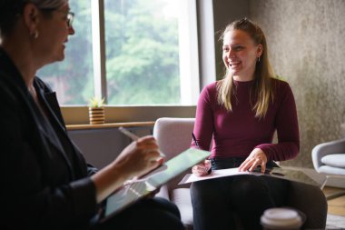 Caucasian businesswoman using digital tablet while brainstorming with female coworker writing on paper at corporate office