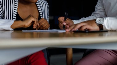 Midsection of multiracial male and female professionals signing business contract on desk while sitting in corporate office