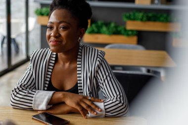 Smiling thoughtful african american young female professional with arms crossed looking away while sitting at table in office cafe