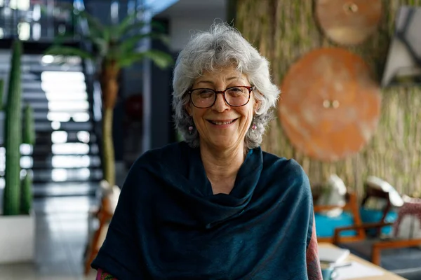 Portrait of smiling senior female professional with gray short hair wearing glasses and scarf standing in corporate office