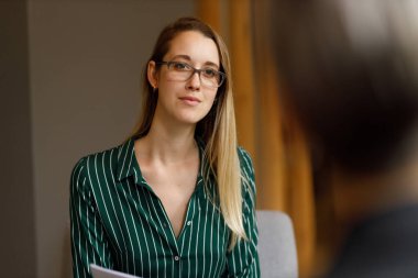 Caucasian young female associate wearing eyeglasses looking and listening attentively to coworker in meeting at office