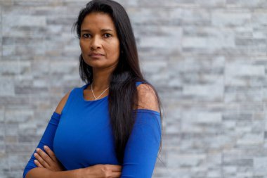 Portrait of confident mixed race female manager with arms crossed looking at camera and standing against wall outside office