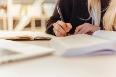 Üniversitedeki kütüphanede okurken genç beyaz kadın ellerinin kitap yazarken sığ derinlik resmini kapat