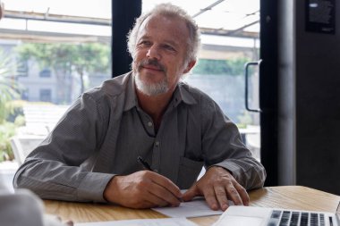 Olgun iş adamı raporlar üzerinde çalışırken ofis toplantısındaki iş arkadaşıyla etkileşime geçiyor