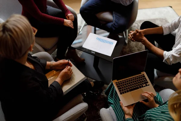 Anonymous business people gathered around a table for a business meeting while using technology and paper diagrams