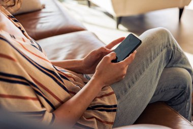 Evdeki koltukta oturan iş kadını cep telefonu kullanıyor. Evde cep telefonuyla çalışan ve işini yöneten bir kadın..