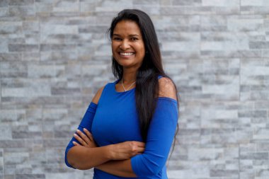 Portrait of confident mixed race female entrepreneur with arms crossed looking at camera and standing against wall outside office