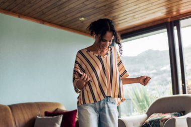 Telefonundan müzik dinleyen ve dans eden güzel bir genç kadın. Afrikalı bir kız müzik dinliyor ve evinde dans ediyor..