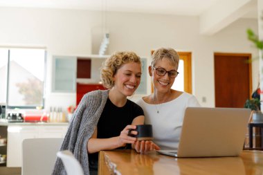 Happy caucasian mother standing by daughter waving hand while talking over video call on laptop at home