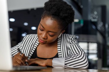 Cheerful african american young female professional laughing and looking away while working in modern corporate office