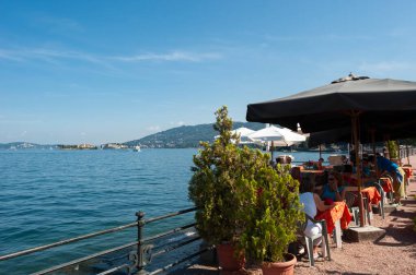 Baveno, Italy - August 17, 2018: Restaurant on the waterfront of Baveno. In the background Lake Maggiore and the Borromean Islands. Baveno is a town in Piedmont in northern Italy