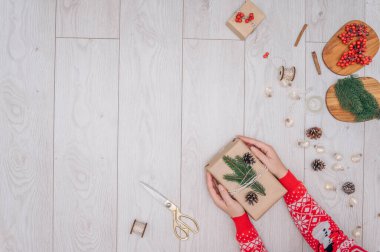 Kahverengi kağıda sarılmış ev yapımı Noel hediyesini tutan üst düzey eller. Şimdiki kutu, ahşap masa dekorasyonu, fotokopi alanı ile üst görünüm