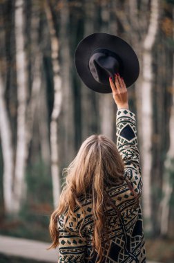 Sonbahar parkında, turuncu yapraklı ağaçların arasında şık, uzun kahverengi paltolu, modaya uygun saç stiline sahip genç bir kadın. İnsanlar, yaşam tarzı, seyahat ve tatil