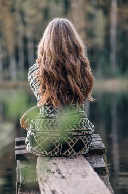 Nehrin kıyısındaki tahta köprüde oturan genç bir kadın. İnsanlar, seyahat, doğa konsepti.