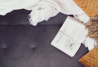 Yatakta beyaz örgü çarşaf, çiçekler ve yastıklarla açılmış bir kitap.