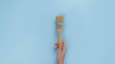 Eldeki boya fırçası mavi arkaplanda izole edildi
