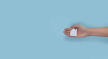 Mavi arka planda minyatür evi tutan kadın elleri. Kopyalama alanı olan üst görünüm. İnşaat, kredi, emlak, konut veya yeni bir konut konsepti satın almak.